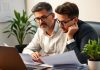 Investor analyzing financial data with laptop and documents.