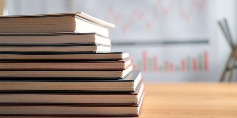 Stack of books with financial charts in background.