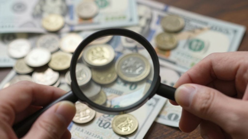 Magnifying glass over coins and banknotes, finance concept.