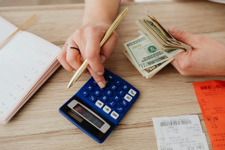 A person using a calculator while holding cash and reviewing receipts, highlighting the financial tradeoffs people overlook when budgeting