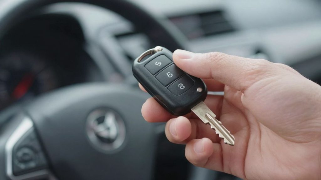 Hand holding car key with new car in background.