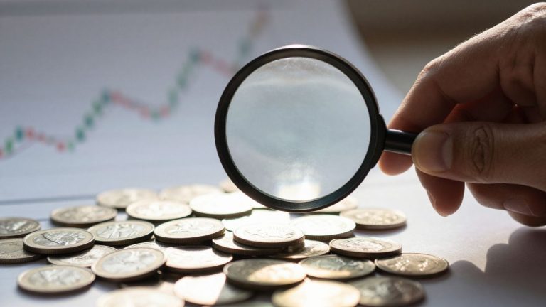 Magnifying glass over coins, financial chart background.